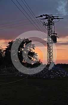 An electricity pylon stands out against the blazing sky of a summer sunset in a remote location