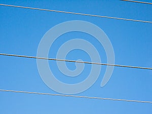 Electricity pylon wires cutting across blue sky background