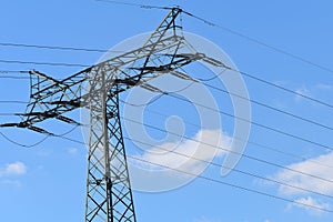 Electricity pylon with wires in front of blue sky with white clouds