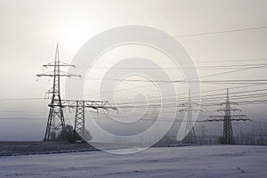 Electricity pylons from distribution power station in foggy winter freeze