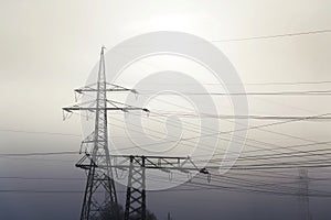 Electricity pylons from distribution power station in foggy winter freeze