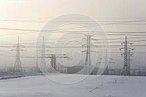 Electricity pylons from distribution power station in foggy winter freeze