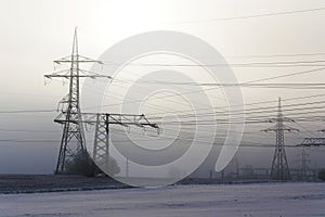 Electricity pylons from distribution power station in foggy winter freeze