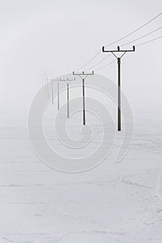 Electricity pylons from distribution power station in foggy winter freeze