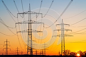 Electricity pylons and electric power transmission lines against vibrant orange sky at sunset. High Voltage towers provide power.