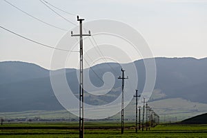 Electricity pylons in row at sunset on green agricultural fields in Transylvania