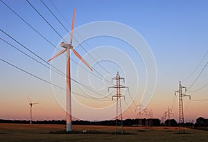 Electricity pylons and wind turbines against sky