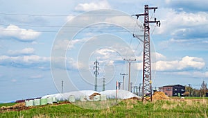 Electricity tower line power grid in countryside meadow hay heap
