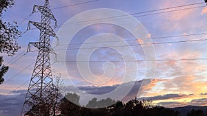 Electricity tower silhouetted against the evening sky with trees below, at sunset