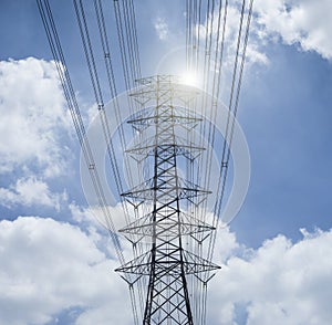 Electricity transmission lines and pylon silhouetted against blue sky and cloud,high voltage tower , light and flare effect added