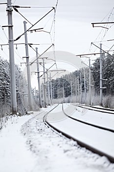 Electrified railway line with poles for wires at winter season, an empty road photo