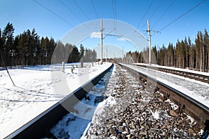 Electrified railway line among wintry forest at sunny day, close-up view at rail-track photo