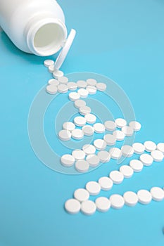 An electrocardiogram made of white tablets with a heart symbol. Blue background. A white pill jar. The concept of cardiac