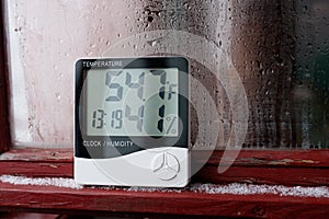 Electronic clock, calendar, thermometer, and hygrometer, against the background of condensation on glass, high humidity. Digital