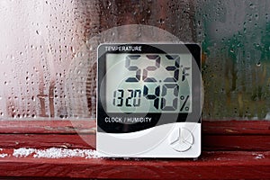 Electronic clock, calendar, thermometer, and hygrometer, against the background of condensation on glass, high humidity. Digital