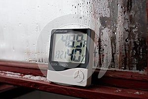 Electronic clock, calendar, thermometer, and hygrometer, against the background of condensation on glass, high humidity. Digital