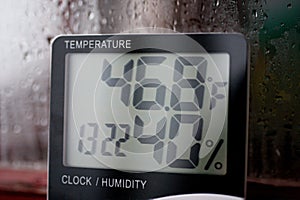 Electronic clock, calendar, thermometer, and hygrometer, against the background of condensation on glass, high humidity. Digital