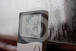 Electronic clock, calendar, thermometer, and hygrometer, against the background of condensation on glass, high humidity. Digital