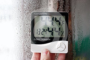 Electronic clock, calendar, thermometer, and hygrometer, against the background of condensation on glass, high humidity. Digital