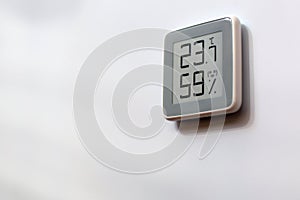 Electronic digital thermometer on white wall showing humidity level, temperature