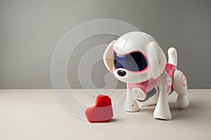 Electronic interactive toy dog puppy with red paper origami heart on a gray background, high technology concept, pet of the future