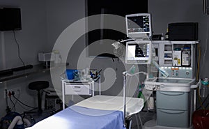 Electronic medical equipment with monitor screens on and empty operating table in operating theatre