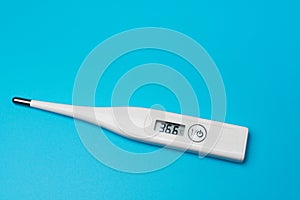 Electronic medical thermometer measuring temperature on blue background. Display shows normal result of the body temperature