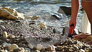 An electronic metal detector on the pebble beach. A man is looking for the luxuries lost by tourists in water and on the