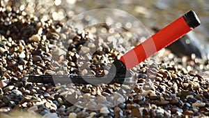 An electronic metal detector on the pebble beach. A man is looking for the luxuries lost by tourists in water and on the