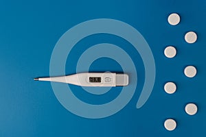 Electronic modern thermometer and medical capsules on a blue background