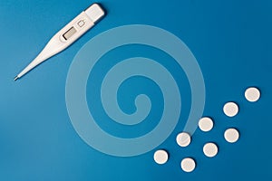 Electronic modern thermometer and medical capsules on a blue background