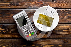 Electronic payments in restaurant. Bank card near aquiring terminal and bill on dark wooden background top view