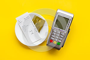 Electronic payments in restaurant. Bank card near aquiring terminal and bill on yellow background top view