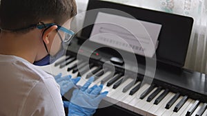 Electronic piano. Fingers press the piano keys. Hands in rubber gloves. Pandemic 2020, self-isolation. Boy in protective gear, mas