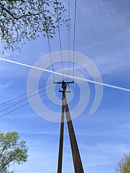 electronic pole with wires against the sky and a white plume from an airplane