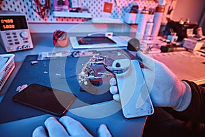 Electronic technician holds a modern smartphone with a broken body, carefully examines the damage using a magnifying