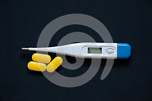 electronic thermometer lies next to yellow pills on an isolated background, medicine and pharmacy, health and treatment