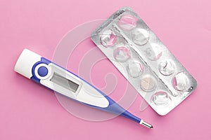 Electronic thermometer and packaging of tablets on a pink background