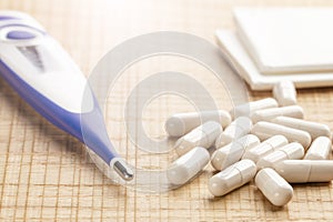 Electronic thermometer and pills with paper handkerchiefs on wooden background