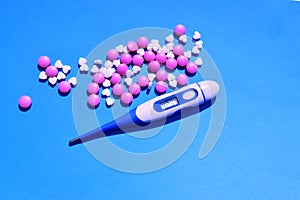 Electronic thermometer, pills or vitamins on a blue background. Protection against viruses, coronaviruses, flu, colds, diseases.