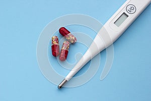 Electronic thermometer and red-yellow pills on a blue background