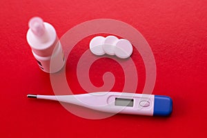 Electronic thermometer, spray and pills on a red background. Means for treating flu and colds, lowering the temperature