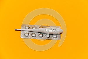 Electronic thermometer with a temperature of 38.6 and pills on a yellow background.