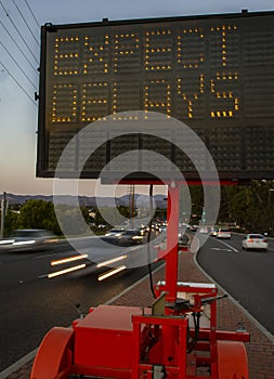 Electronic traffic sign stating Expect Delays with traffic blurred at rush hour