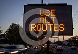 Electronic traffic sign stating Use Alternate Routes with blurred traffic photo