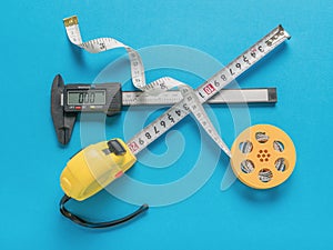 An electronic vernier caliper, a reel with measuring tape and a tape measure on a blue background