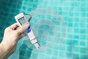 Electronic water testing meter in girl hand over blurred blue swimming pool water background, summer outdoor day light
