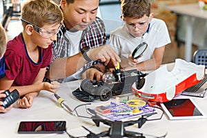 Electronics engineer teacher with young european students working together with a radio controlled car model. Soldering