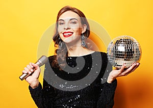 Elegance brunette woman with long curly hair dressed in evening dress holding disco ball and microphone