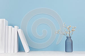 Elegance home decor - white books and small glass vase with dried flowers on soft light white wood table and blue background.
